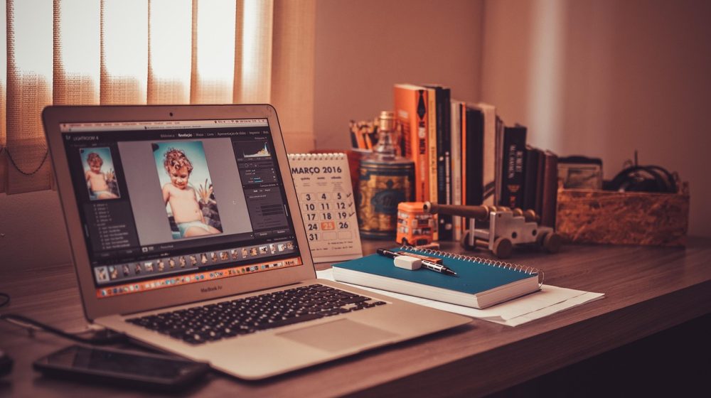 书桌上一台笔记本电脑播放着经典老番画面，旁边摊开的笔记本写着按年份排列的补番清单，暖色台灯照亮桌面